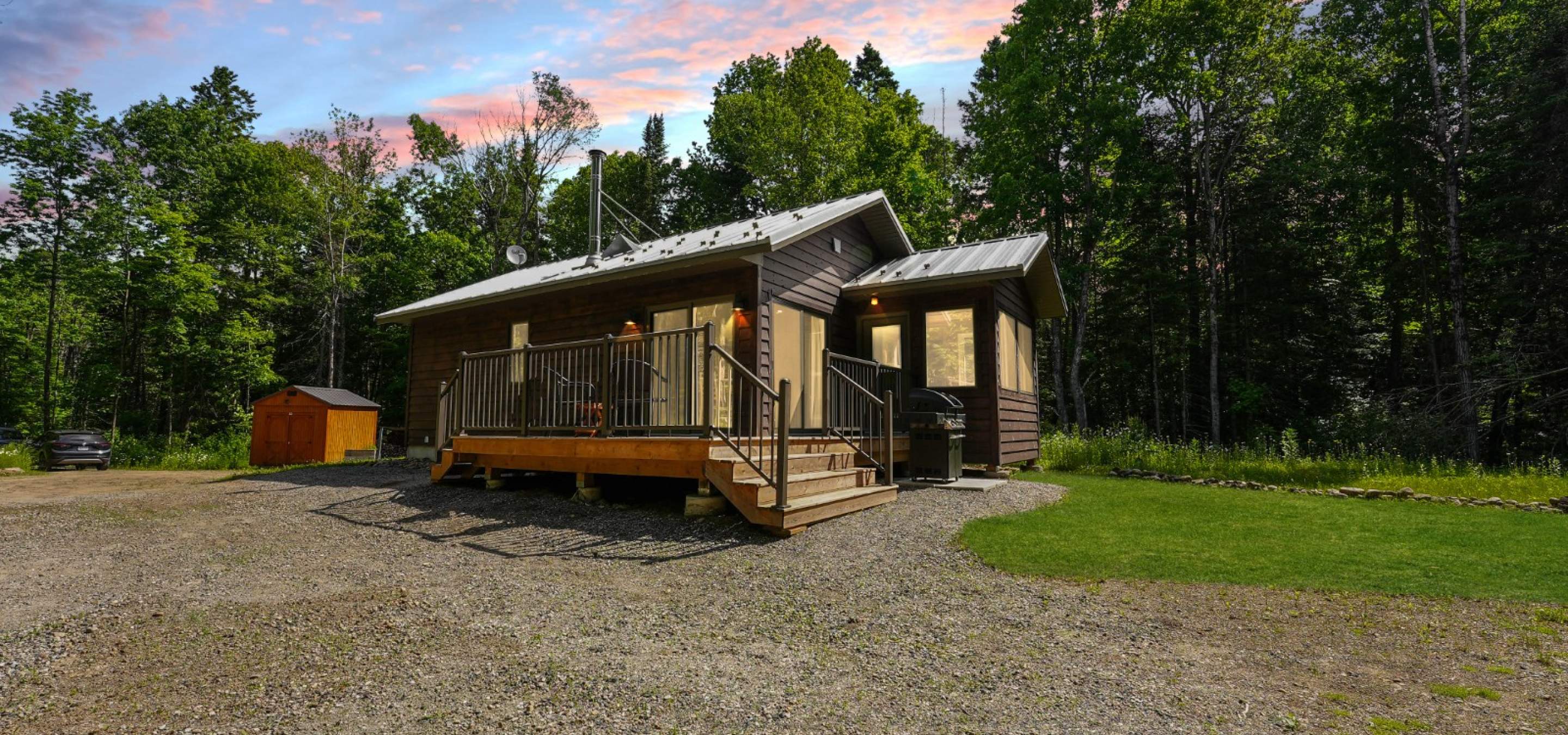 grey home with deck in front and gravel laneway