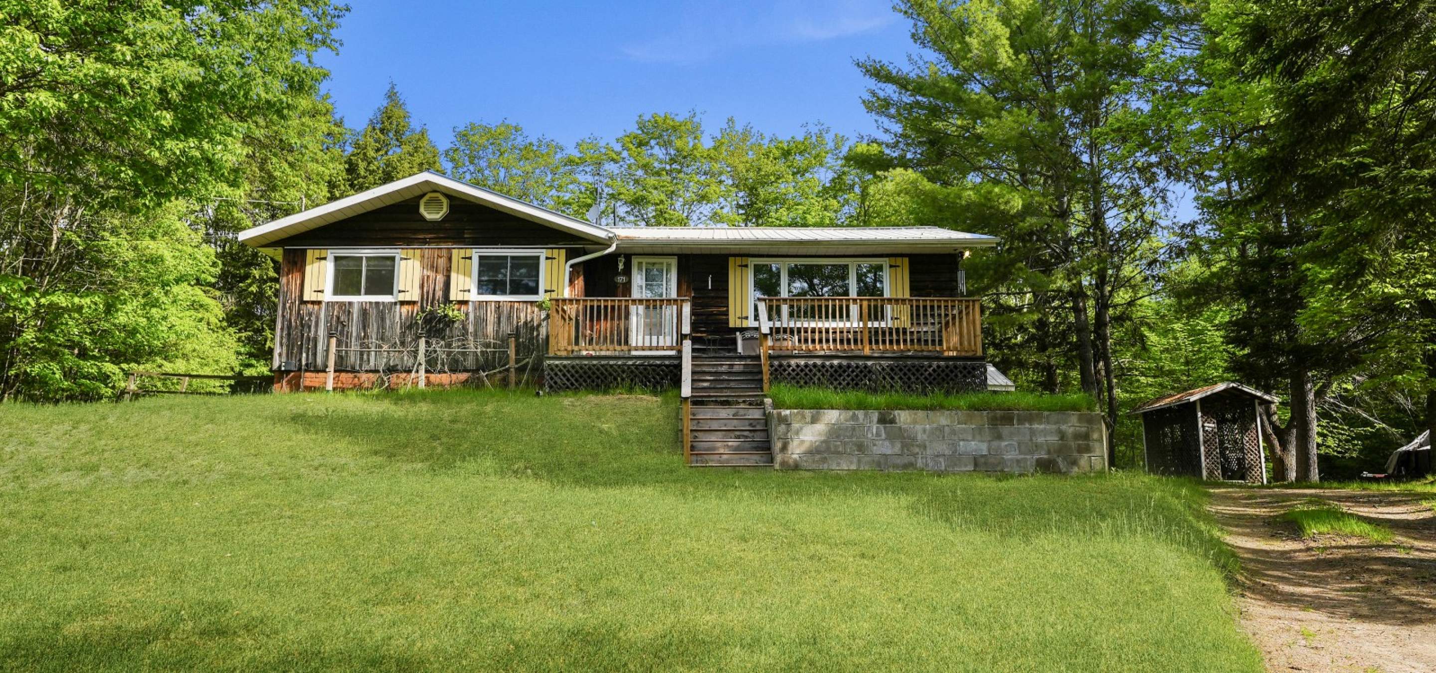 home on a slight hill, stairs leading up, green grass, wood siding and yellow shutters