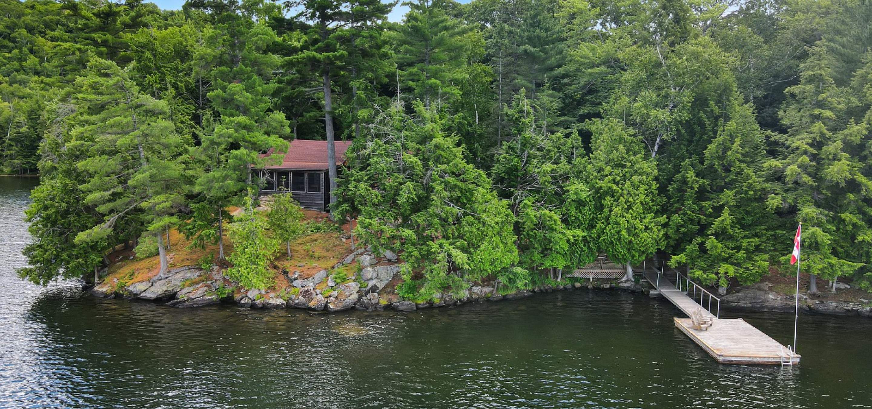 Cabin sits atop a rocky point surrounded by cedar and pine trees with a boat dock to the right