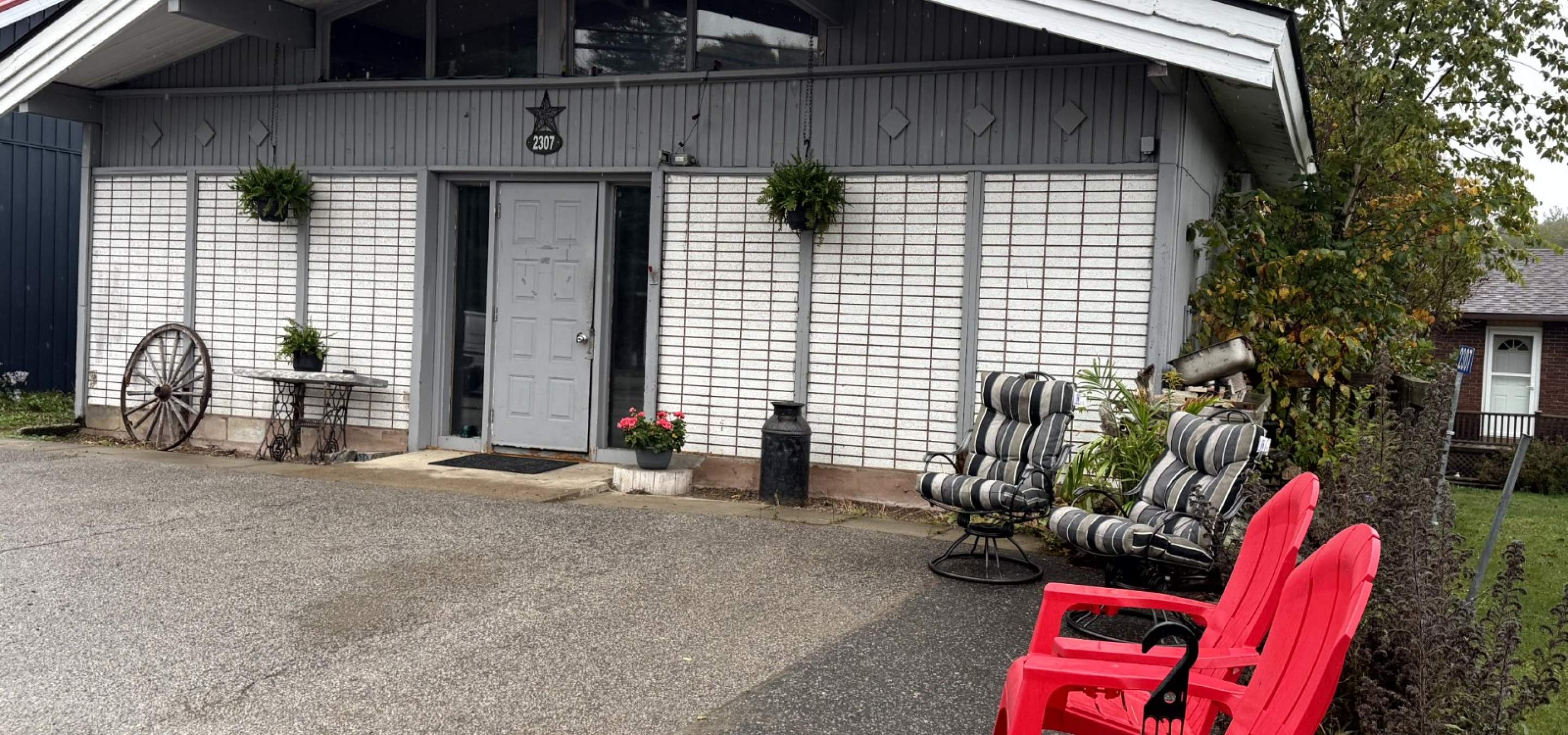 White and grey home with 2 red muskoka chairs and 2 striped chairs sitting out front.