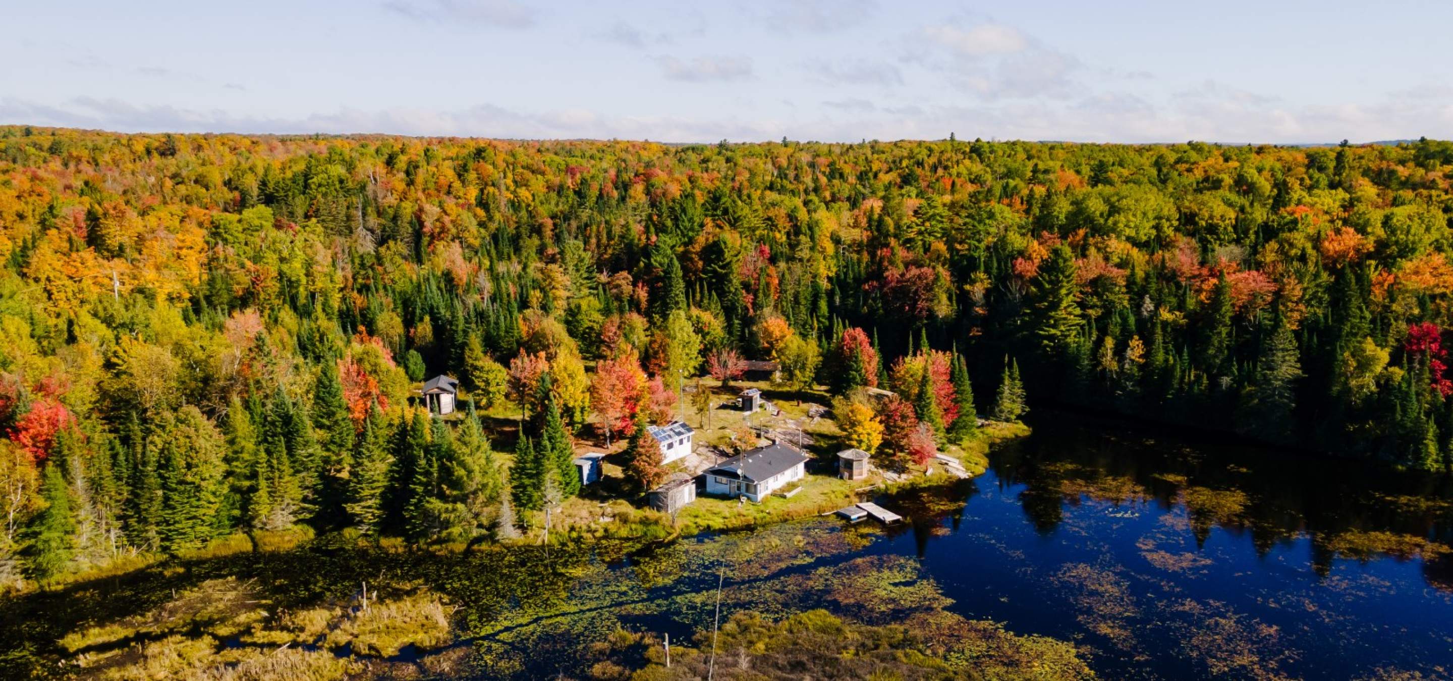 white home in front of a body of water with forest behind and clear blue skies