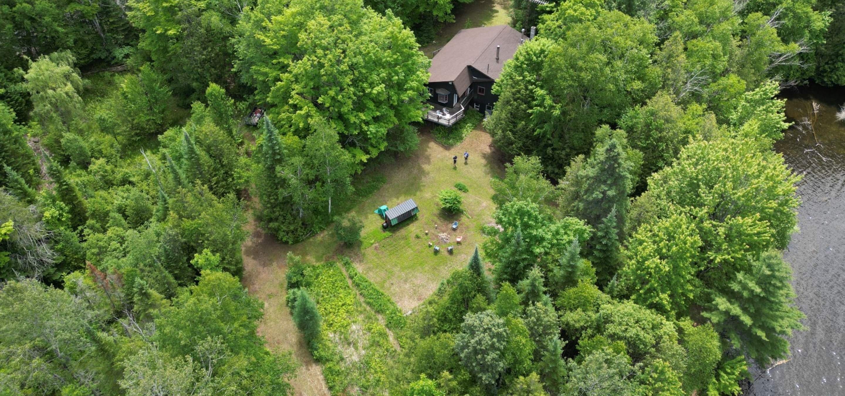 Aerial view of a cottage surrounded by trees with a lake 