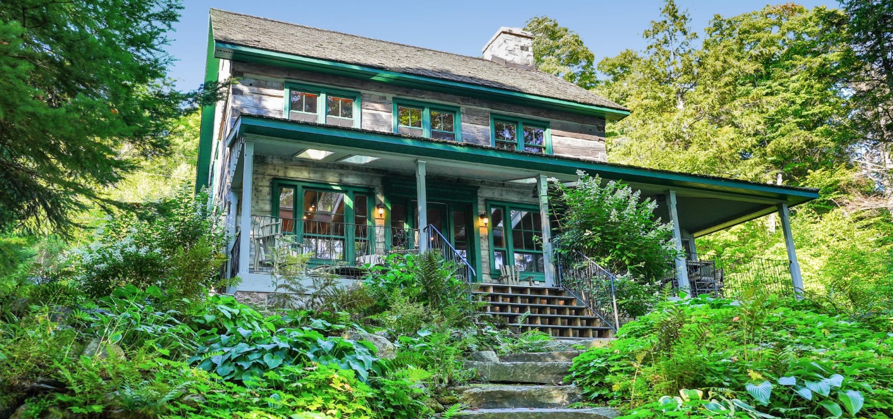 two storey home with covered front porch and surrounded by greenery.