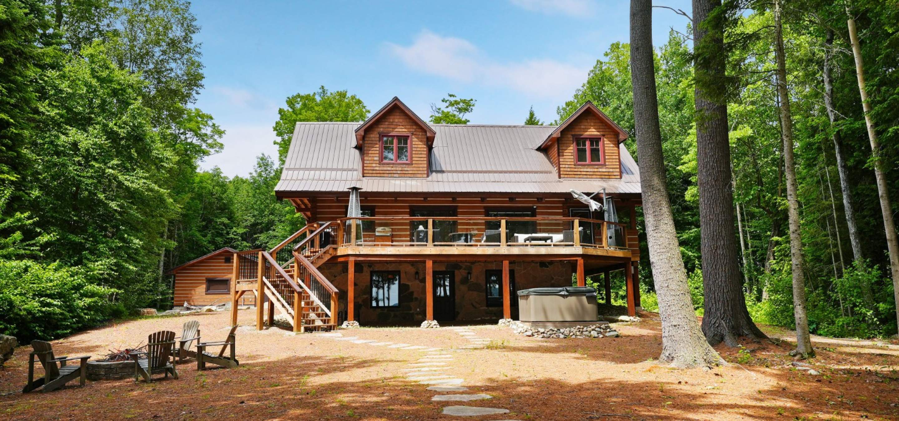 two storey log home with a path leading away and a fire pit on the side with 4 chairs