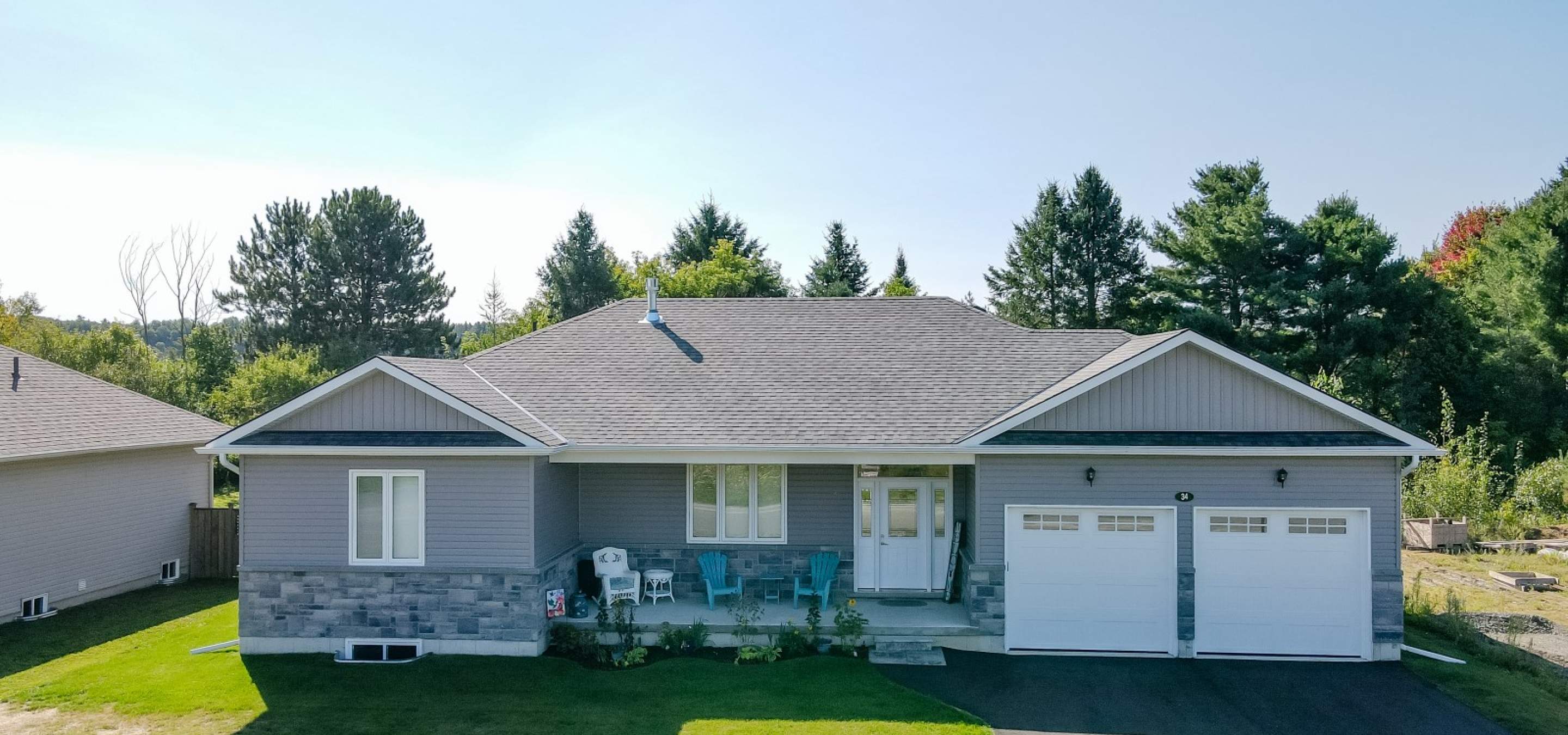 Residential home clad in stone and vinyl, white double garage doors and adirondack chairs on a covered porch.