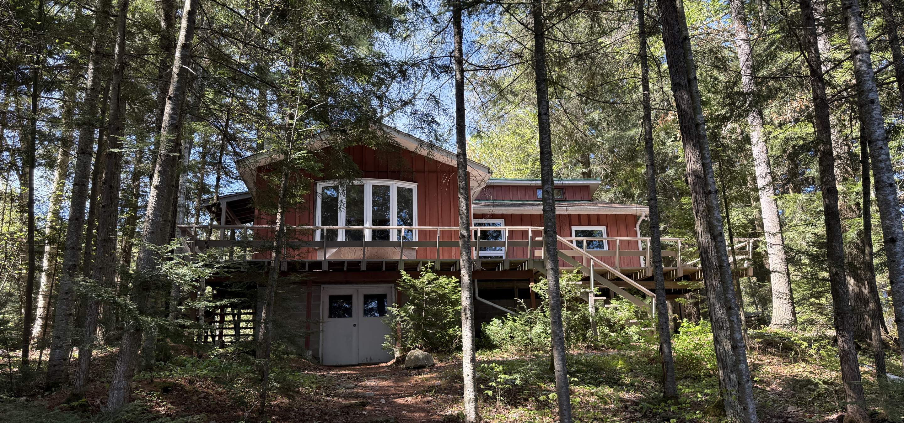 cottage with deck and white door under the deck. surrounded by trees