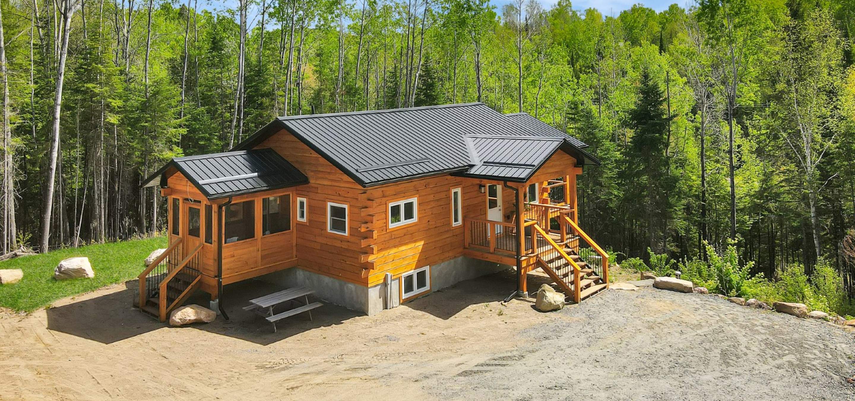 log home with 2 flights of stairs up, green trees and blue sky