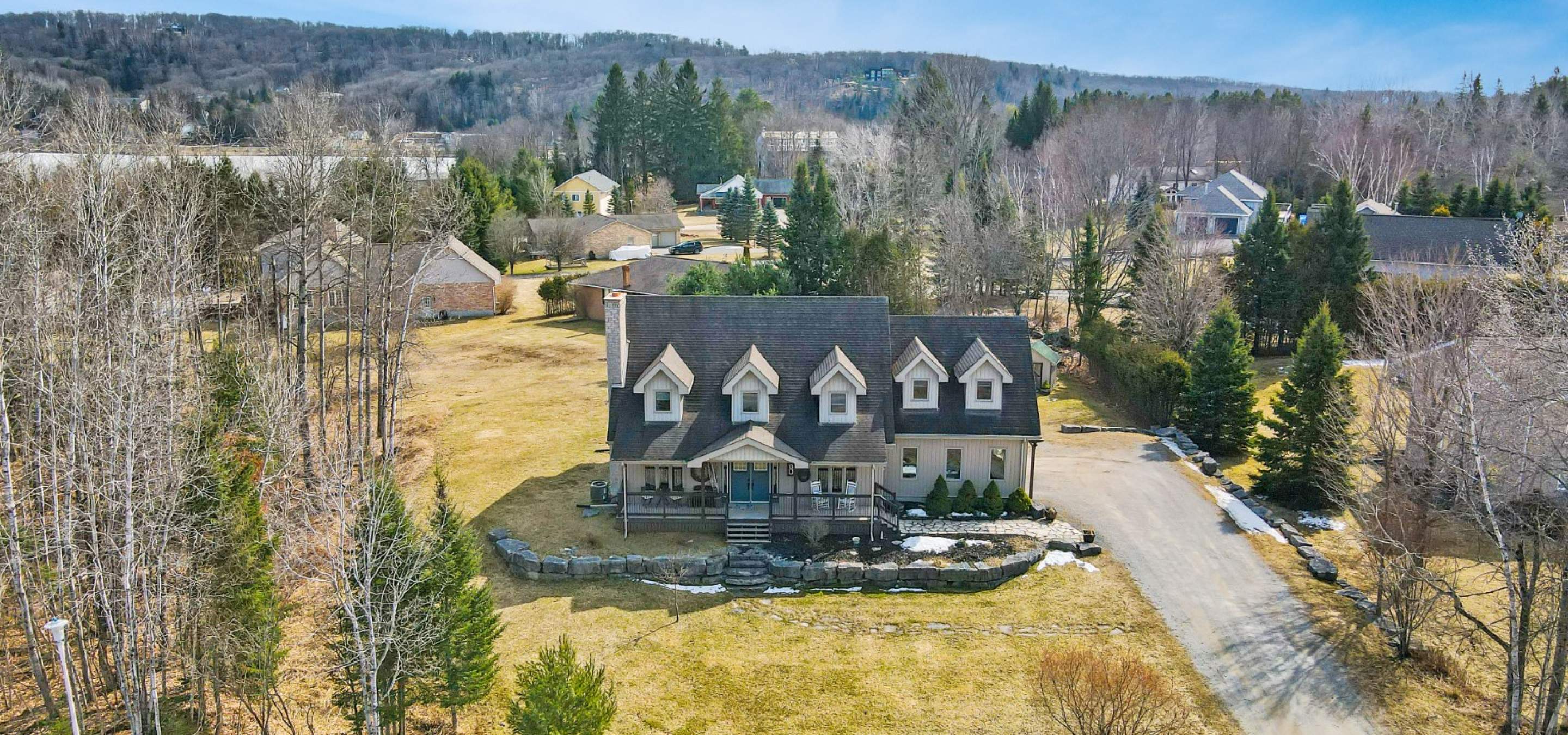 Home with 5 second floor domers and covered front porch, surrounded by grass and trees