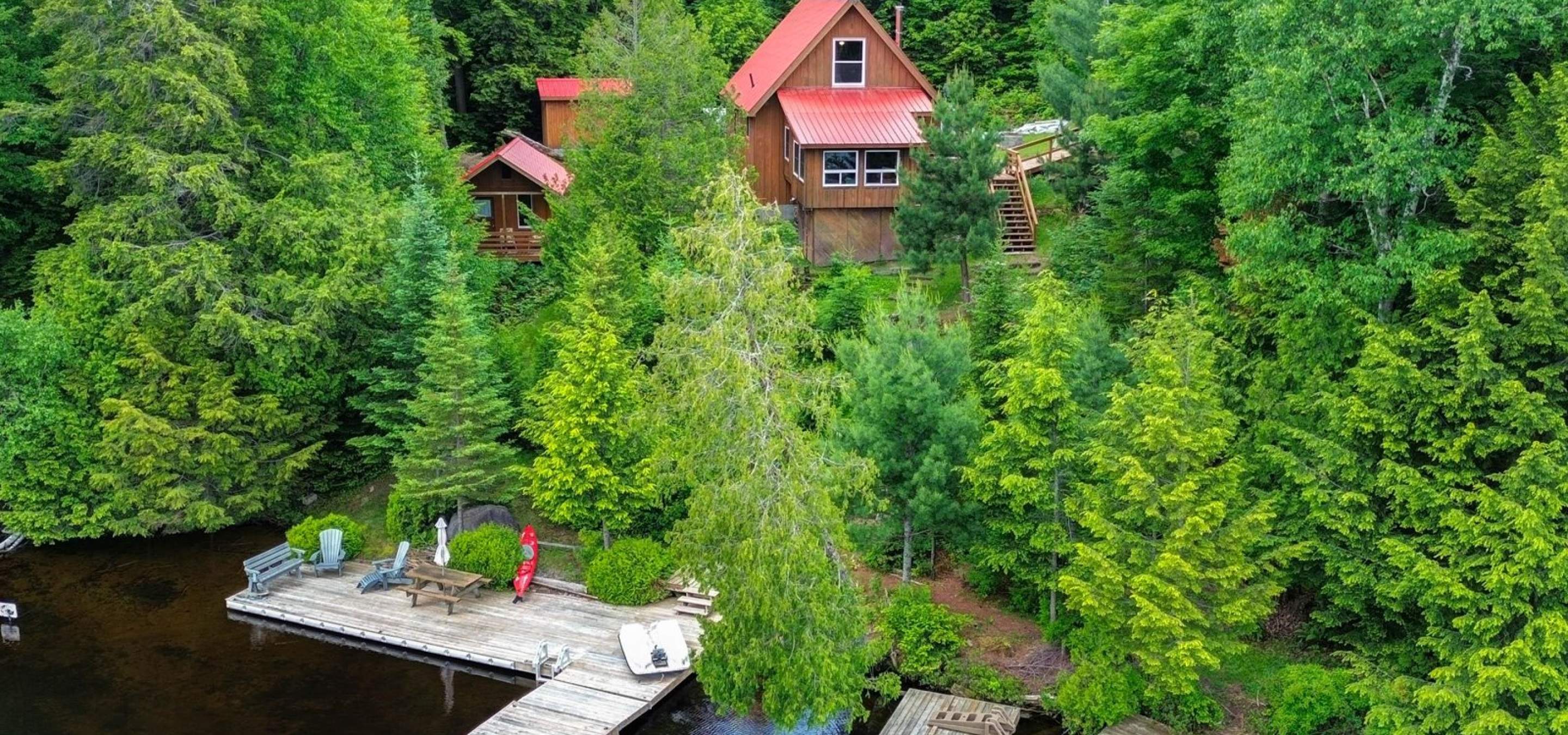View of a cottage from the lake, surrounded by trees, with a cottage that has a red roof