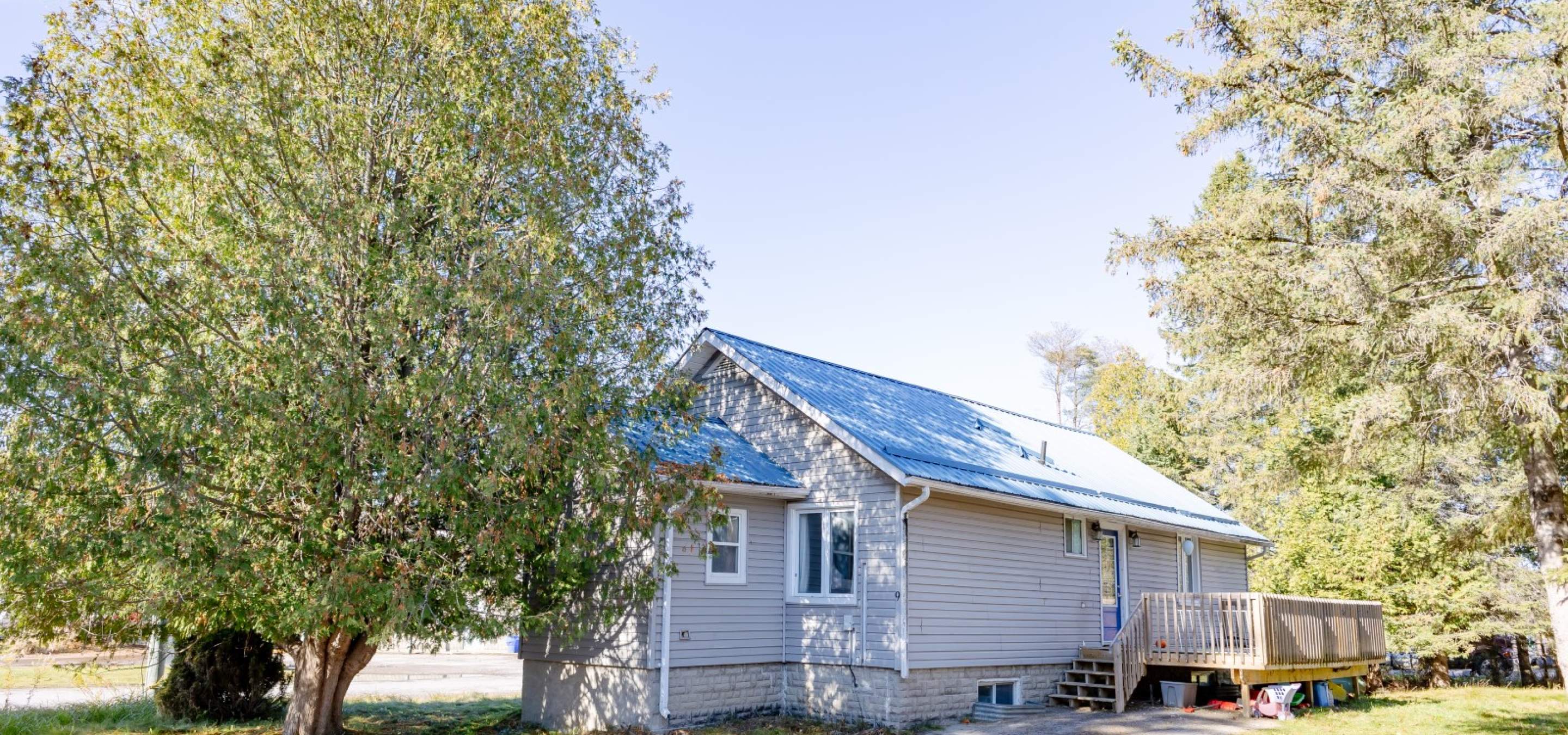 bungalow with blue metal roof, green grass, trees and blue sky.