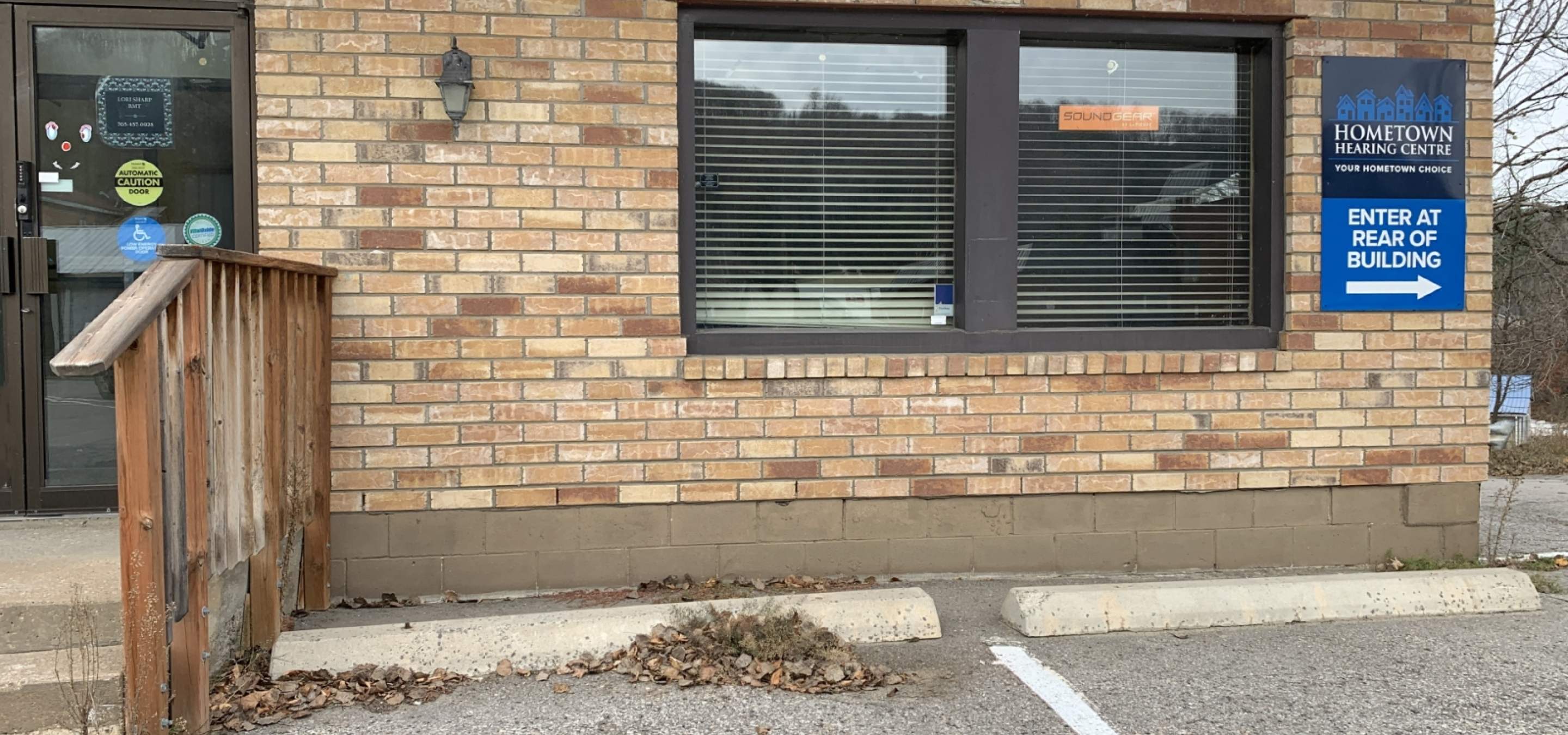 Brick commercial business front with door, double window, railing and parking spot with curbs.
