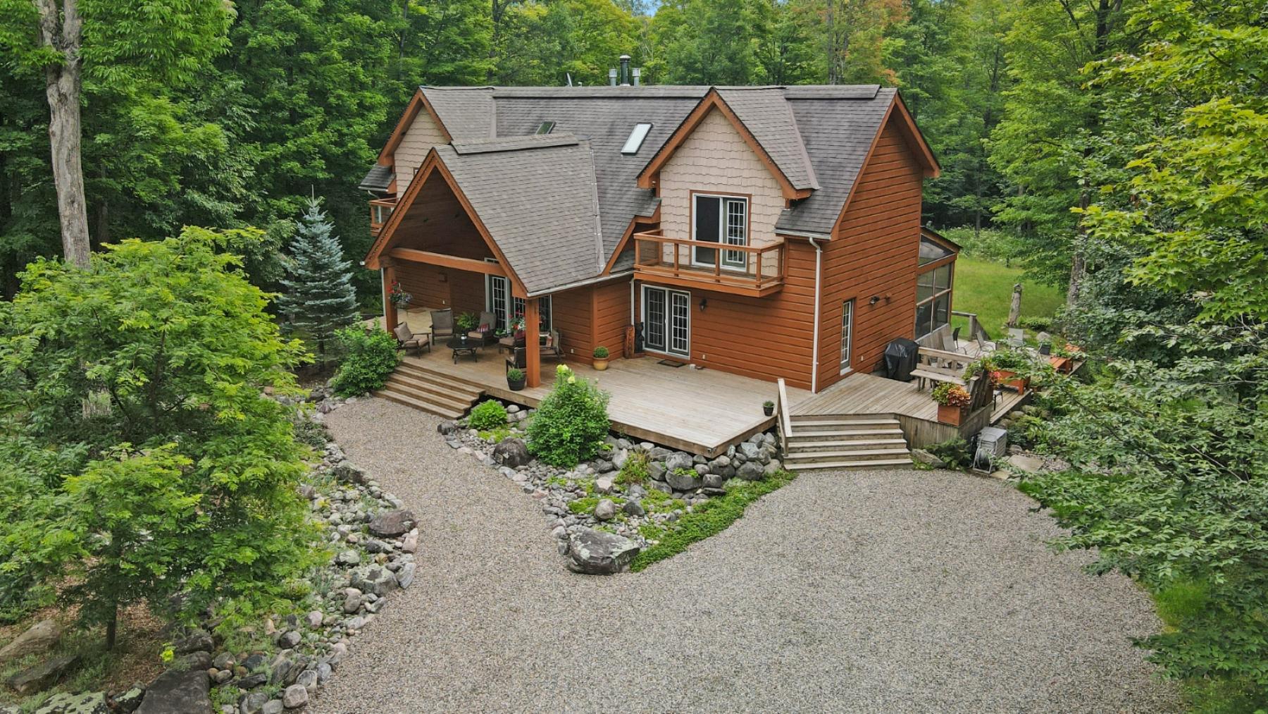2 story home with a large, partially covered front porch. Gravel laneway and walk way, surrounded by grass and tress.