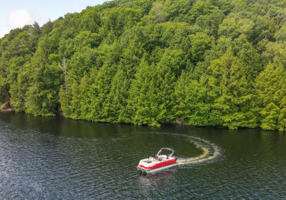 A red and white boat driving on the lake in front of a 10-acre treed building lot.