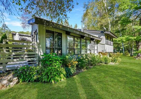 Grey home with bushes out front and green grass.