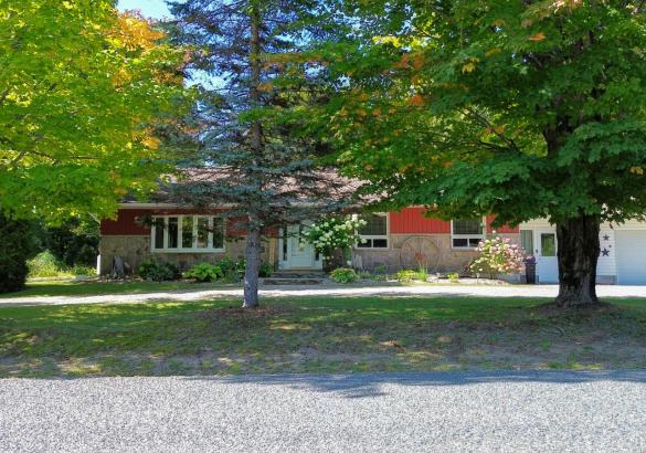red and stone house hidden behind trees with a white garage