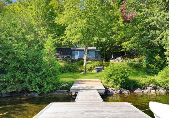 View from a dock in the lake looking at a Blue cottage behind trees around it