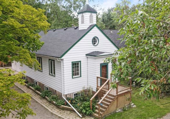 White church style home surrounded by trees and stairs leading to front porch