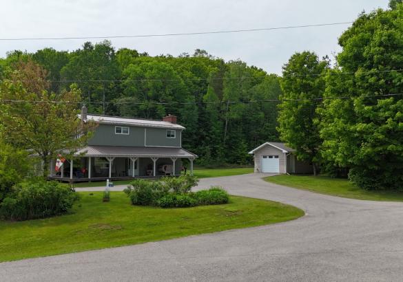 Grey house with full covered porch, detached garage with white door and paved laneway