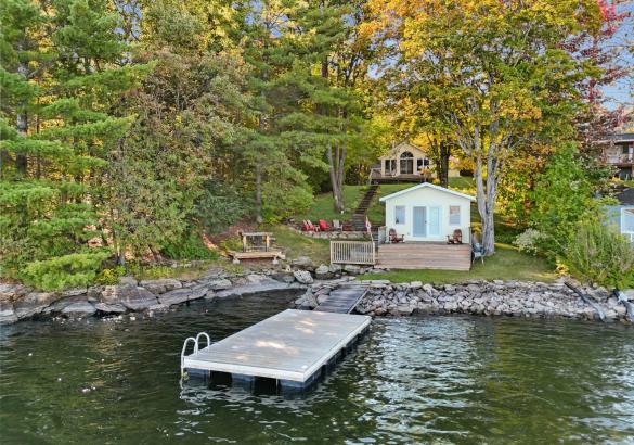 Cottage hidden behind trees, yellow boathouse at the lake, dock in the lake. 