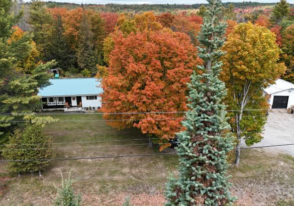 Home with white siding and brown wood siding, white garage on the right, and fall coloured trees.