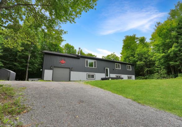 Grey home, single garage door, green grass and gravel laneway