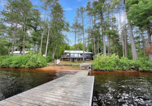 View of a gray cottage from standing on the dock, sandy beach