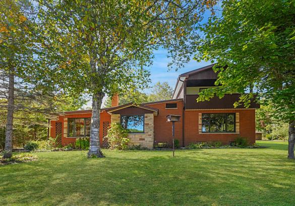 Red brick house shaded by tree and green grass.