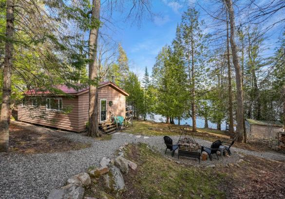 View of the back of a cottage with stone path leading to chairs around a fire and lake in the back