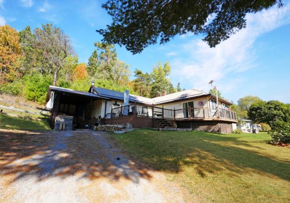 off white home with large front deck and gravel laneway
