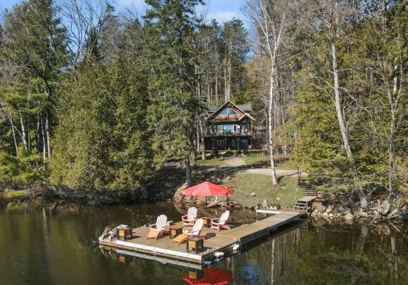 Cottage among trees, dock in the lake, red umbrella on dock