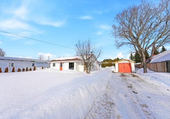 white bungalow with a red door, garage with red door, snow on the ground, blue skies