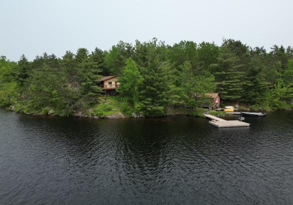 aerial view of cottage in trees with a dock in the water 