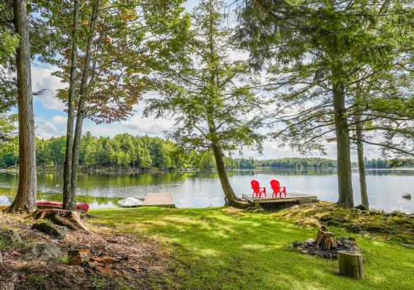 2 red muskoka chairs sitting on a dock over looking the lake with trees and grass behind them