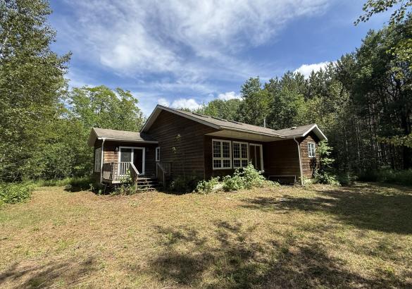 Brown house with small deck, brown grass and trees.