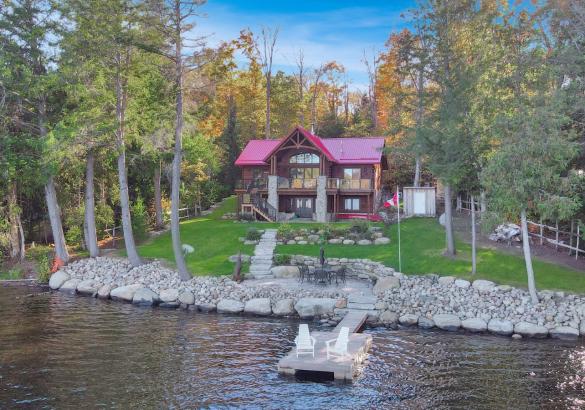 log home with red roof, green grass lawn, rock line before the lake. 