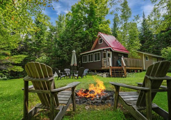 Cabin with red roof and 2 chairs sitting in front of a fire