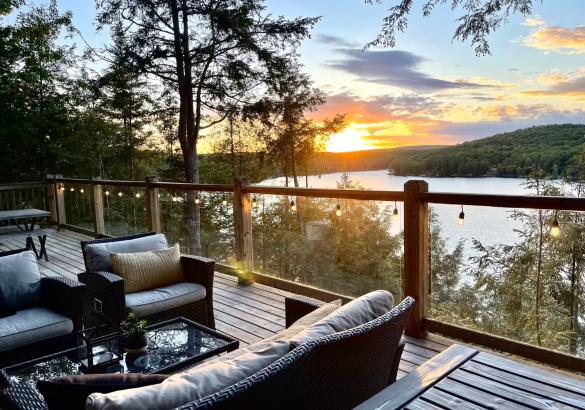 View of the lake with a sunset. Glass railing and 2 chairs, and a couch on the deck.