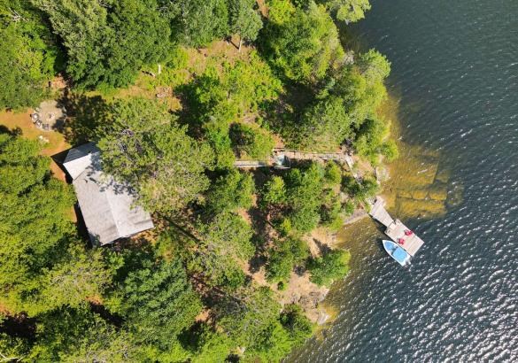 Forested point lot with dock and boat in the water, cottage roof and stairs to the lake