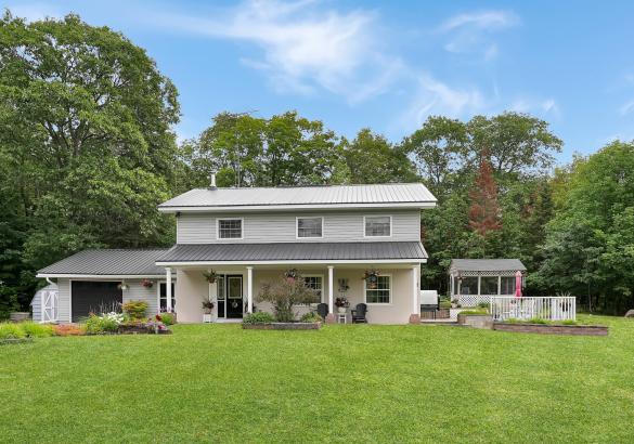 two storey white home with attached single garage with black door and a screen gazebo