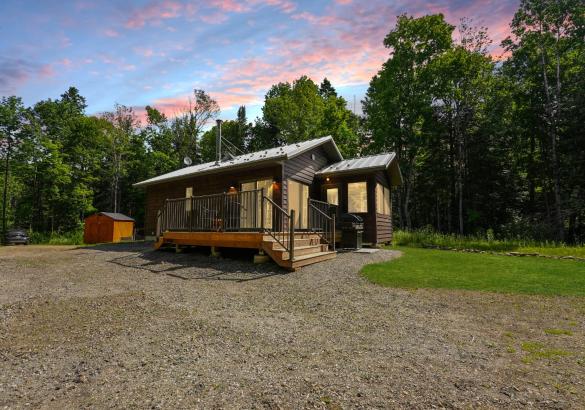grey home with deck in front and gravel laneway