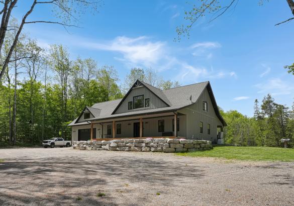 grey house with a covered front porch, stone retaining wall, gravel in front and blue skies