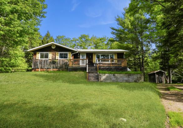 home on a slight hill, stairs leading up, green grass, wood siding and yellow shutters
