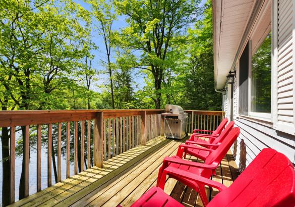 4 red muskoka chairs on a deck overlooking the lake through trees.