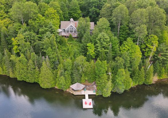 Home atop a forested hill with a gazebo deck and dock with 2 red muskoka chairs at the lake below