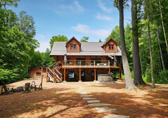 two storey log home with a path leading away and a fire pit on the side with 4 chairs