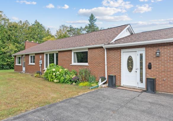 Red brick home with attached double car garage with paved laneway in front. Surrounded by grass and trees.