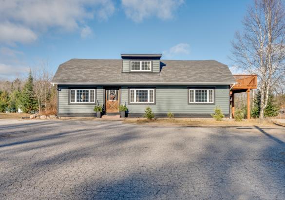 green house with wood door, 2 planters, wood deck off the side and paved parking in front.