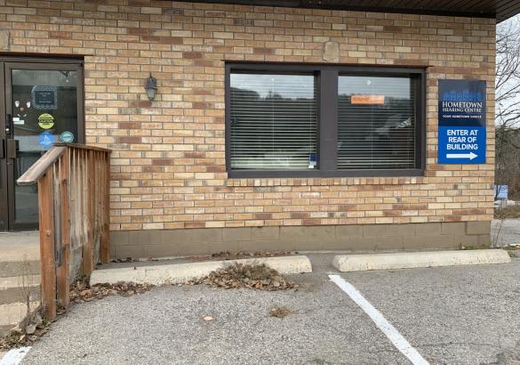 Brick commercial business front with door, double window, railing and parking spot with curbs.